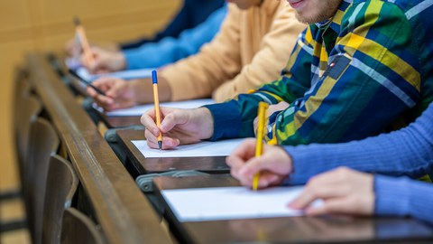The picture shows five students sitting next to each other in a lecture hall taking an exam.