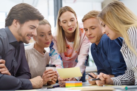 Abbildung einer Gruppe von 5 Studierenden, die sich gemeinsam einen Zettel anschauen