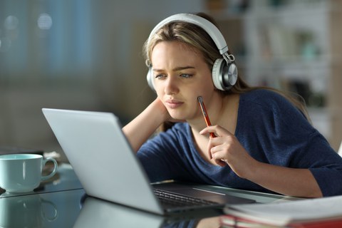 junge Frau schaut konzentriert in Laptop und trägt Kopfhörer.
